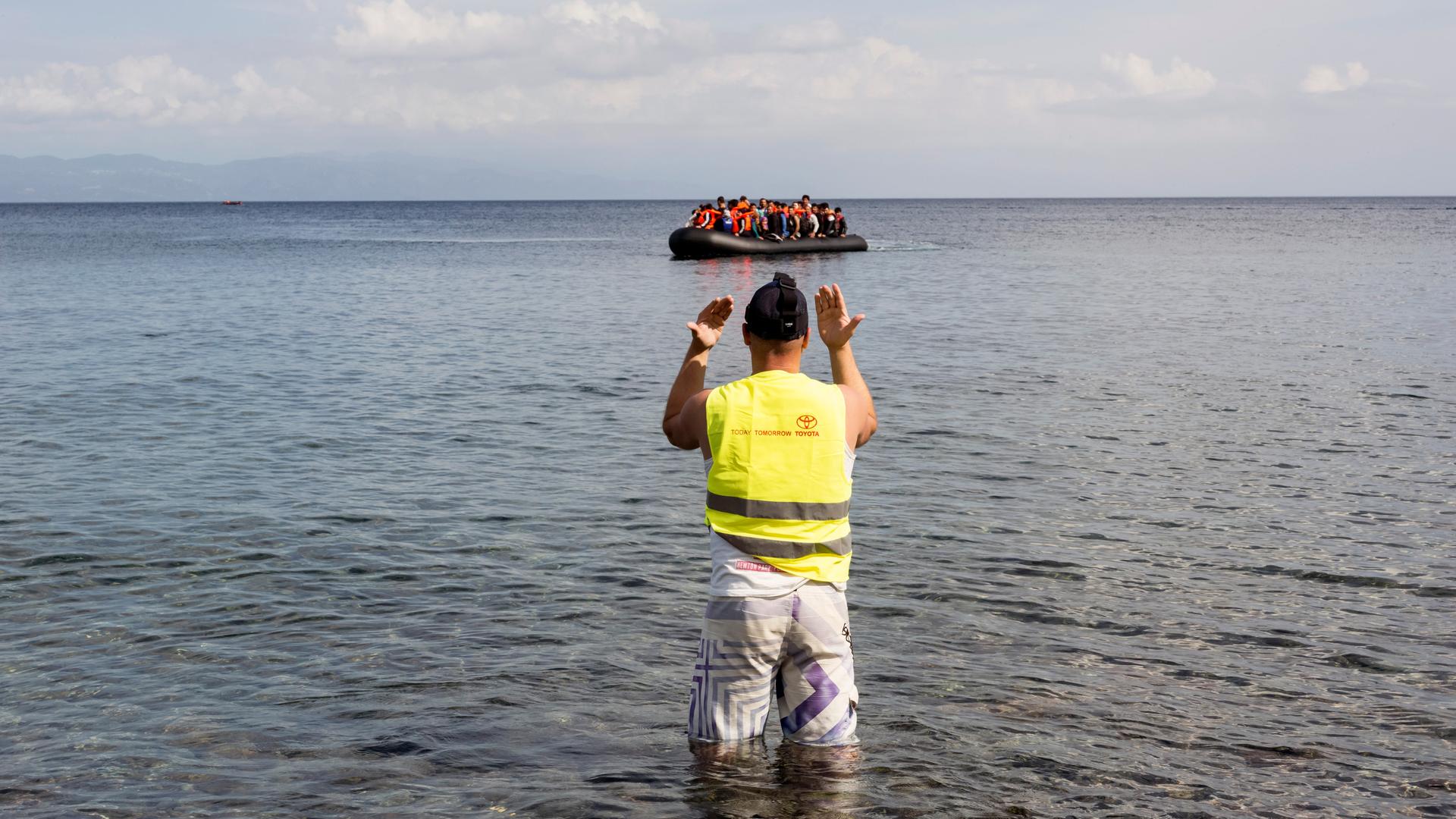 Ein mit Migranten besetztes Schlauchboot wird nach der Überquerung der Ägäis von der Türkei aus an die Küste von Lesbos von einem Mann mit gelber Warnweste an Land gewunken.