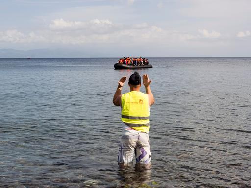 Ein mit Migranten besetztes Schlauchboot wird nach der Überquerung der Ägäis von der Türkei aus an die Küste von Lesbos von einem Mann mit gelber Warnweste an Land gewunken.