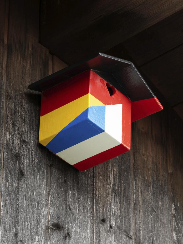 Ein Nistkasten für Vögel in den Farben der deutschen und französischen Nationalflagge hängt an unter einem hölzernen Dachgiebel. 