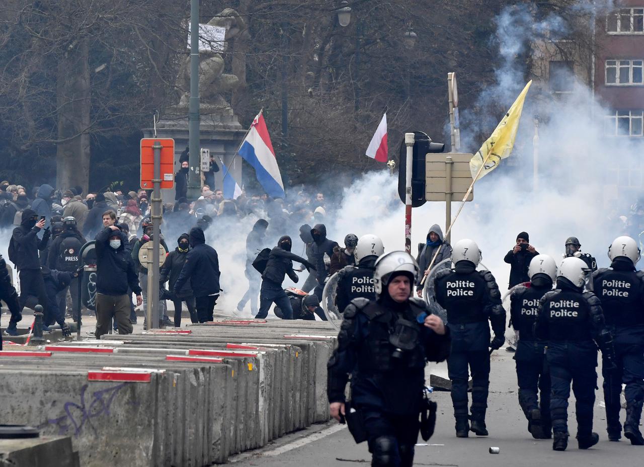 Polizisten in Schutzkeidung, im Hintergrund schwarz gekleidete Menschen; einige von ihnen schwenken die niederländische Flagge.