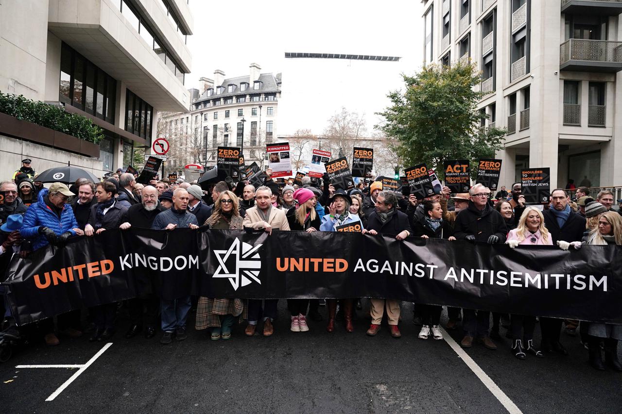 Die Teilnehmer marschieren geschlossen durch eine Straße in London. Sie halten Plakate in die Höhe und tragen ein Banner vor sich her, auf dem "Das Vereinigte Königreich  - vereint gegen Anitisemitismus" steht.