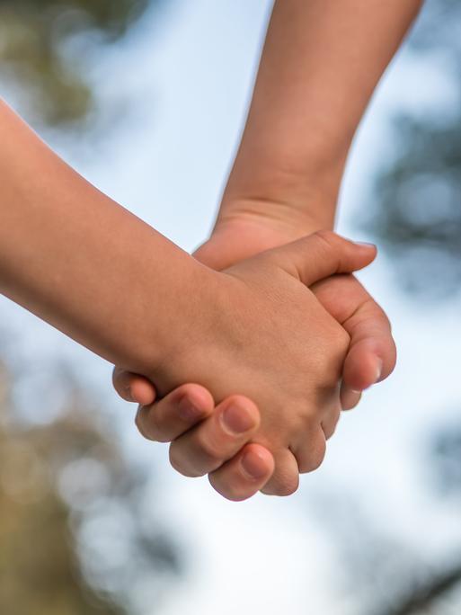 Zwei Hände halten sich, im Hintergrund ist verschwommen Blätter zu sehen Zwei Hände halten sich, im Hintergrund ist verschwommen Blätter zu sehen