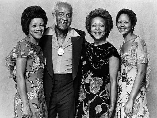 Auf dem Bild sind vier Schwarze Menschen zu sehen, die in die Kamera lächeln, es handelt sich um die Staple Singers. 