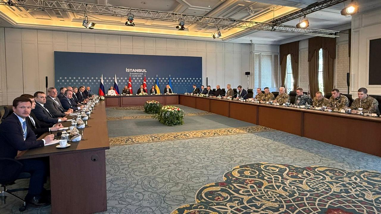 In einem großen Sitzungssaal sitzen sich Vertreter der ukrainischen und der russischen Verhandlungsdelegation an Tischen gegenüber.