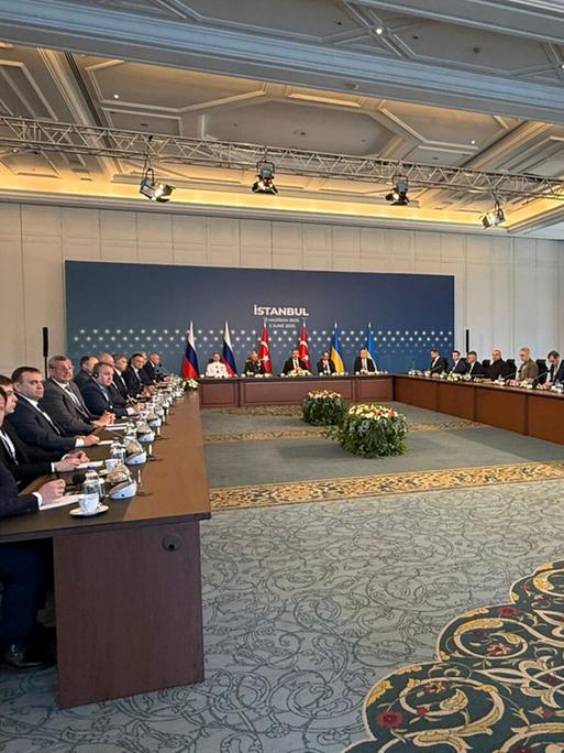 In einem großen Sitzungssaal sitzen sich Vertreter der ukrainischen und der russischen Verhandlungsdelegation an Tischen gegenüber.