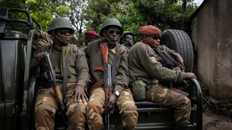 Mehrere Soldaten in militärischer Montur sitzen auf einem LKW. Alle tragen Sonnebrillen und schauen ernst.