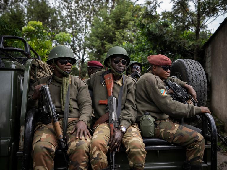 Mehrere Soldaten in militärischer Montur sitzen auf einem LKW. Alle tragen Sonnebrillen und schauen ernst.