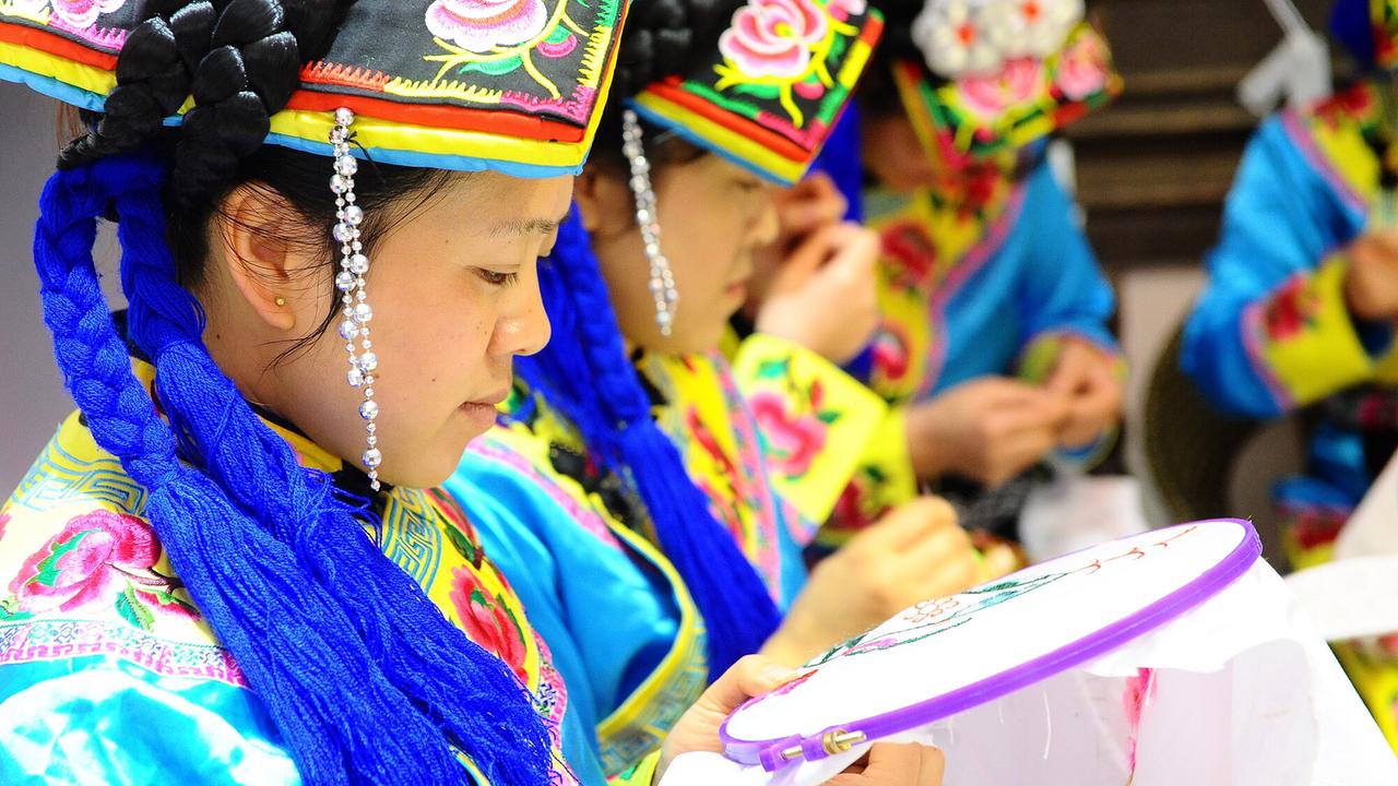 Frauen in sehr farbenfrohen Trachten fertigen Stickereien.