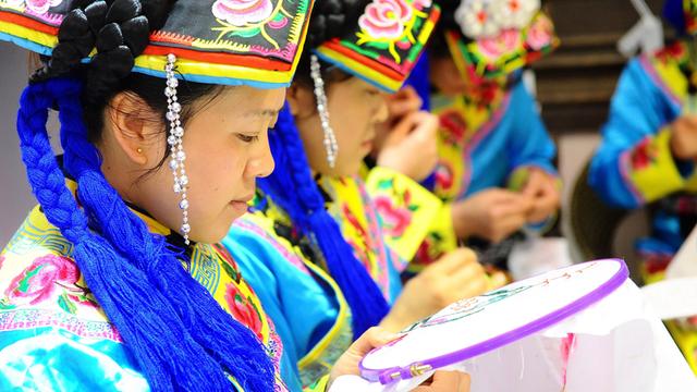 Frauen in sehr farbenfrohen Trachten fertigen Stickereien.