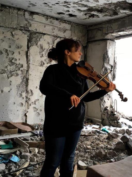 Eine Frau spielt Geige in einem zerstörten Haus.