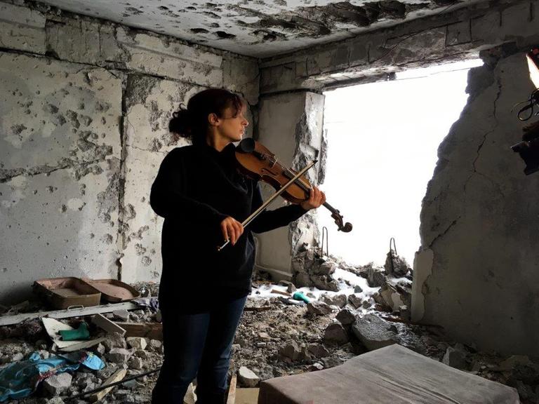 Eine Frau spielt Geige in einem zerstörten Haus.