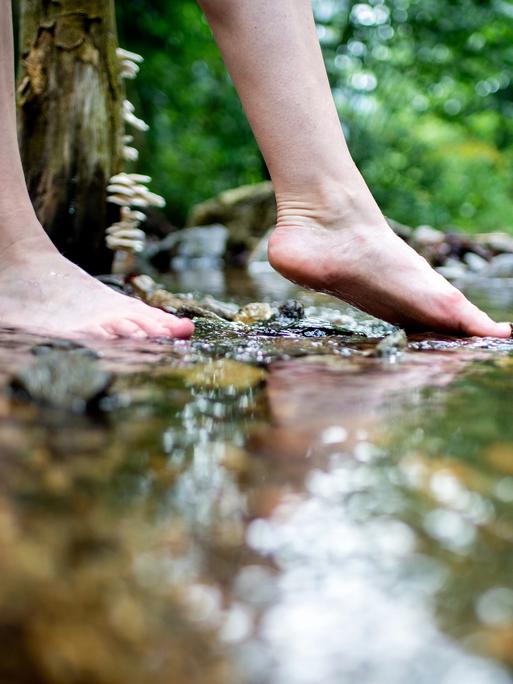 Eine junge Frau erfühlt das Flussbett eines Bachs mit den Füßen