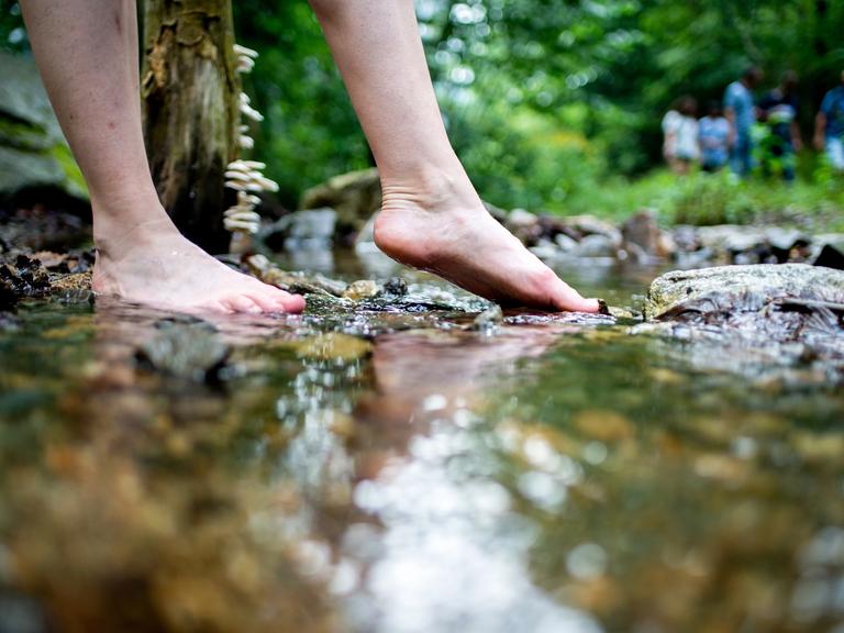 Eine junge Frau erfühlt das Flussbett eines Bachs mit den Füßen