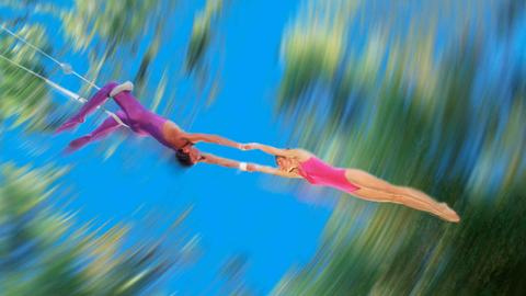 Verschwommenes Bild zweier Trapezkünstler: Ein männlicher Trapezartist hält eine Trapezkünstlerin.