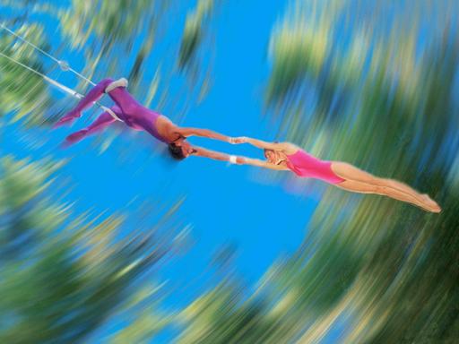 Verschwommenes Bild zweier Trapezkünstler: Ein männlicher Trapezartist hält eine Trapezkünstlerin.