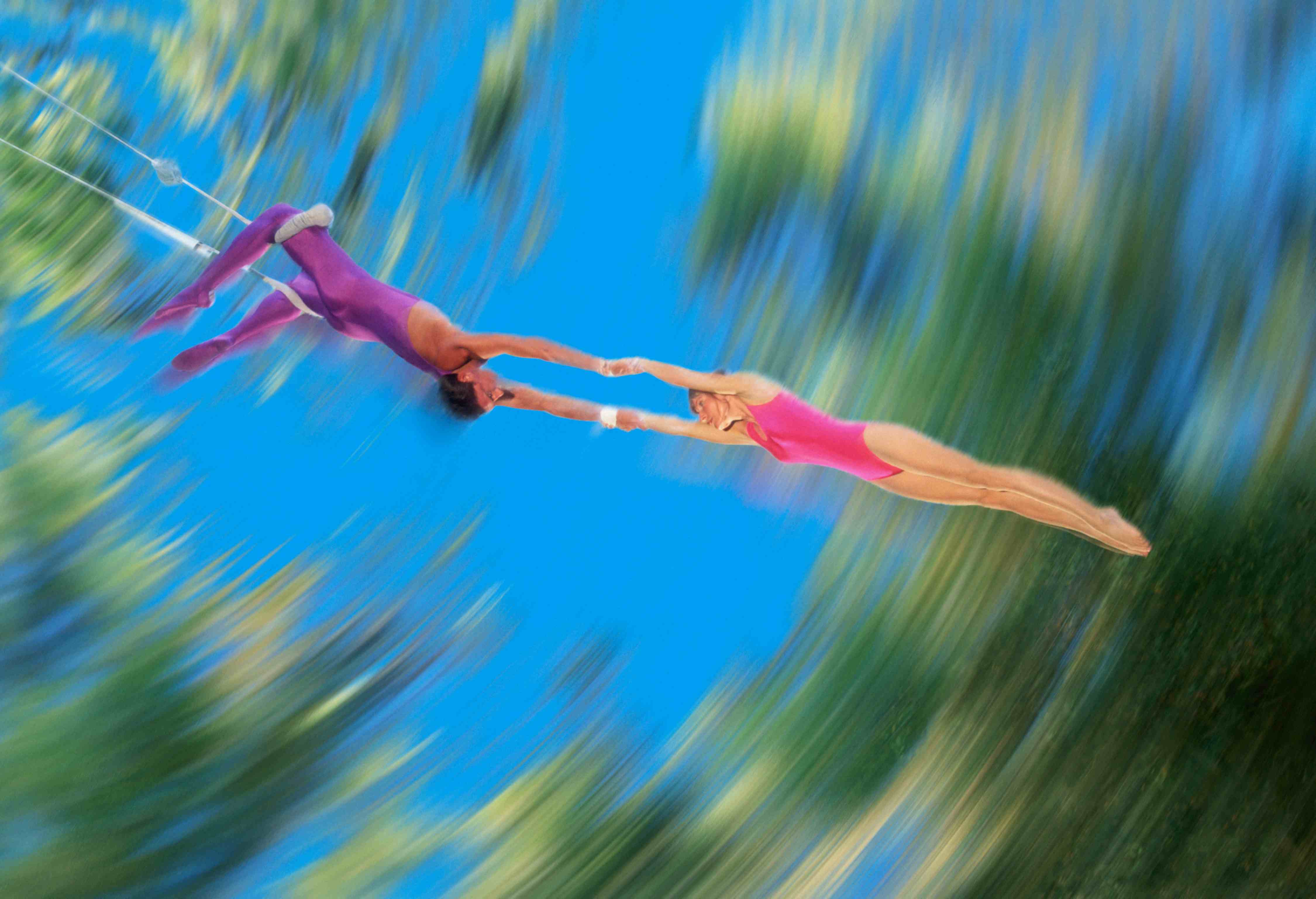 Verschwommenes Bild zweier Trapezkünstler: Ein männlicher Trapezartist hält eine Trapezkünstlerin.