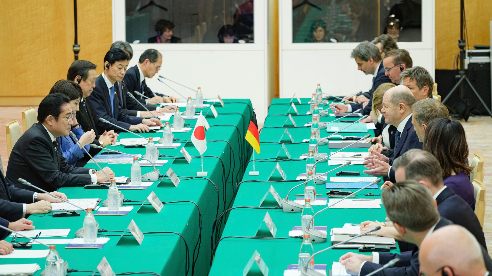 Das Foto zeigt Mitglieder der deutschen und der japanischen Regierung. Die Delegationen sitzen sich gegenüber an grünen Tischen. Unter den Teilnehmern sind Bundeskanzler Olaf Scholz und Japans Premierminister Fumio Kishida.