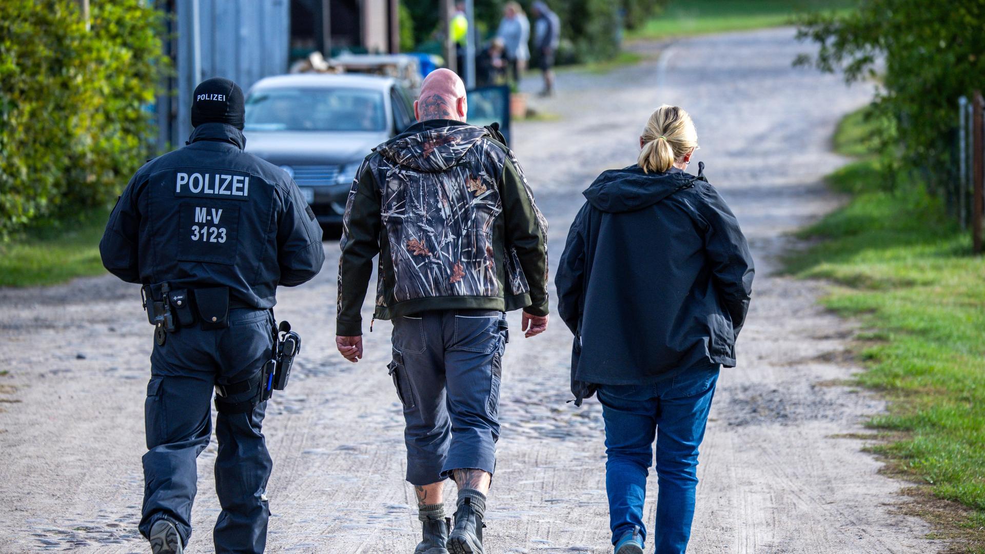Zwei Beamte begleiten den bundesweit bekannten Rechtsextremisten Sven Krüger (Mitte) über dessen Grundstück in Jamel.