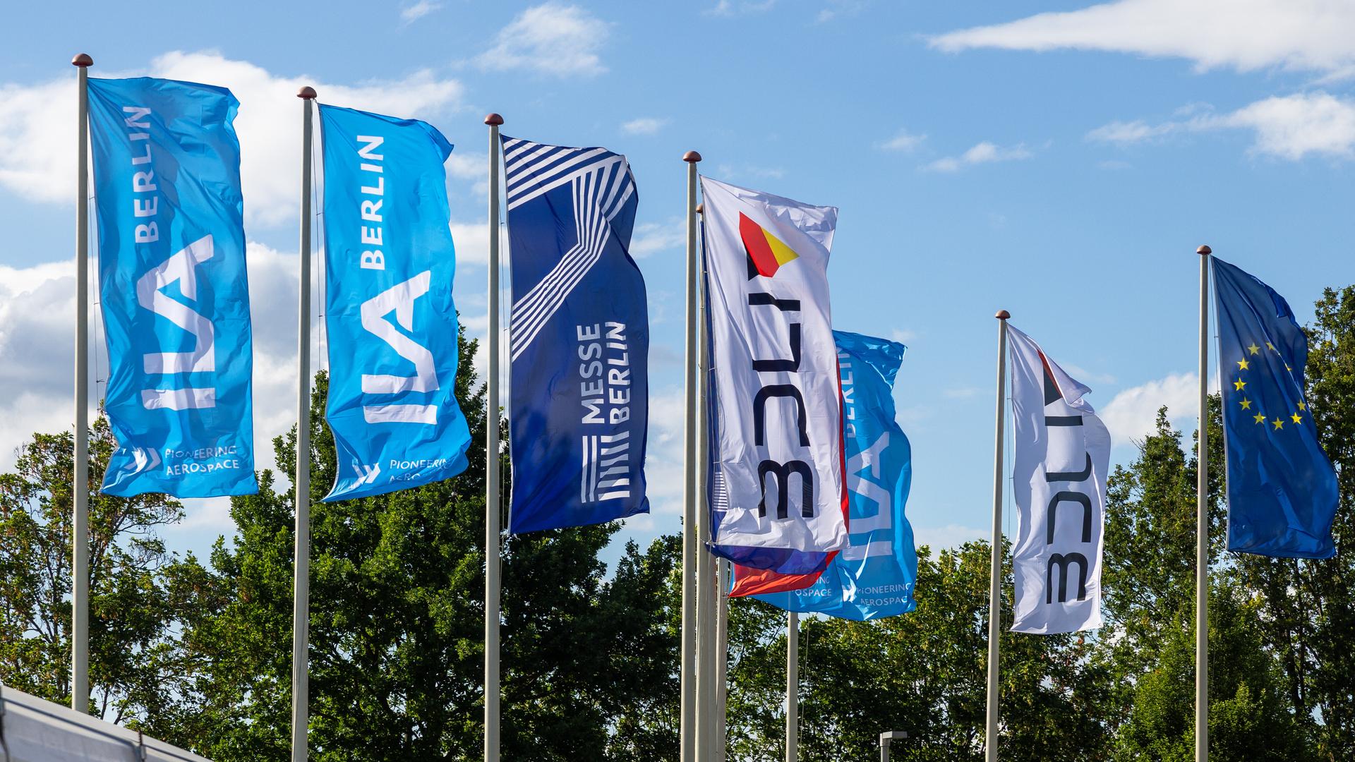 Fahnen der ILA Berlin (Internationale Luft- und Raumfahrtausstellung) und der Messe Berlin wehen im Wind. Daneben ist die Europaflagge zu sehen.
