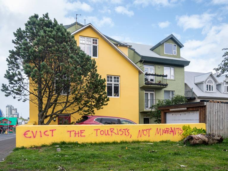 Der Slogan "Evict the tourists not the migrants" ("Die Touristen ausweisen, nicht die Migranten") steht auf einer Mauer eines Wohnhauses in Reykjavik, Island 2023.