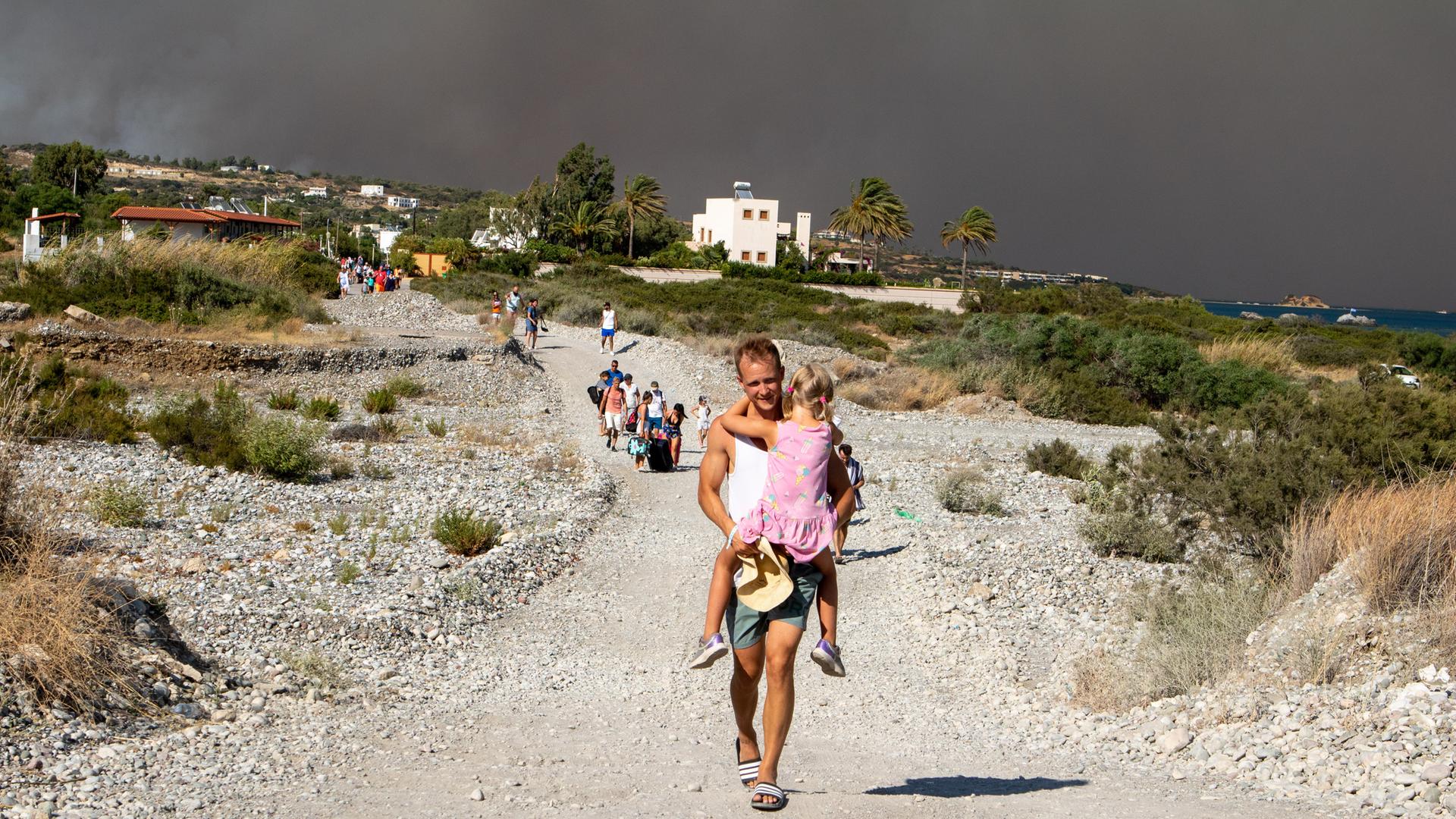 Ein Tourist trägt ein Mädchen auf einer Landstraße auf seinen Armen während sie sich aus ihrem Hotel in Sicherheit vor den Waldbränden auf Rhodos bringen. 