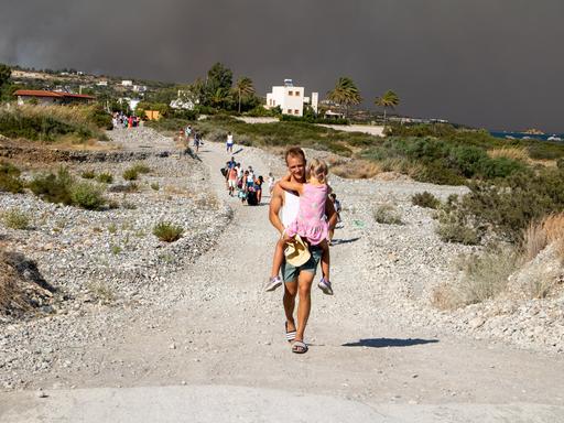 Ein Tourist trägt ein Mädchen auf einer Landstraße auf seinen Armen während sie sich aus ihrem Hotel in Sicherheit vor den Waldbränden auf Rhodos bringen. 