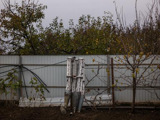 Streubombenträger, gesammelt auf den Feldern im Dorf Zelenyj Hai in der Ukraine, lehnen an einer Wand vor Obstbäumen.