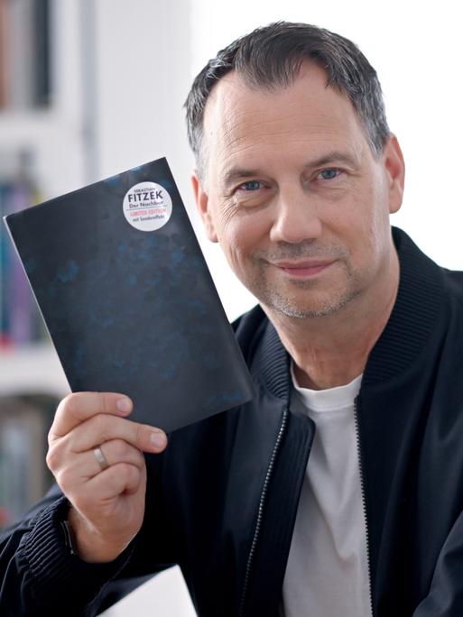 Sebastian Fitzek hält ein Buchcover hoch, auf dessen Rückseite ein Button mit seinem Namen klebt.