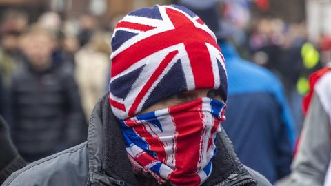 Ein Mann vermummt sich mit der englischen Union Jack, Mütze und Mundschutz. Demonstranten versammeln sich am 25. Januar 2026 in Crowborough, auf einem ehemaligen Militärgelände, in dem Asylanten untergebracht werden sollen.