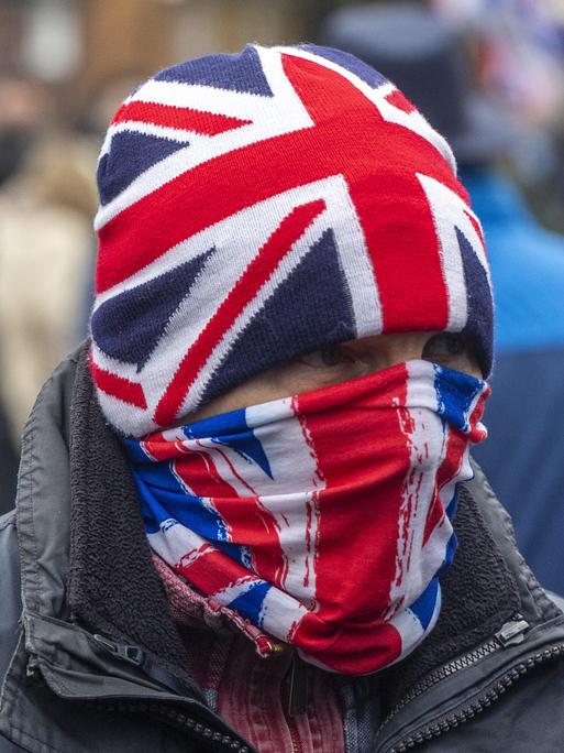Ein Mann vermummt sich mit der englischen Union Jack, Mütze und Mundschutz. Demonstranten versammeln sich am 25. Januar 2026 in Crowborough, auf einem ehemaligen Militärgelände, in dem Asylanten untergebracht werden sollen.