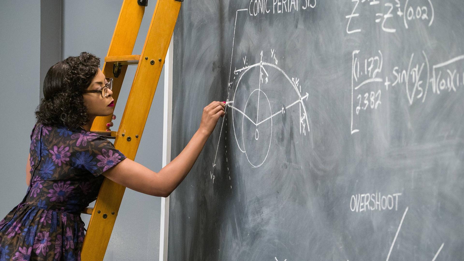 Szene aus dem Film "Hidden Figures". Katherine Johnson trägt Hornbrille und ein für die Sechziger Jahre typisches Kleid. Sie steht auf einer Leiter und berechnet Flugbahnen auf einer Tafel.