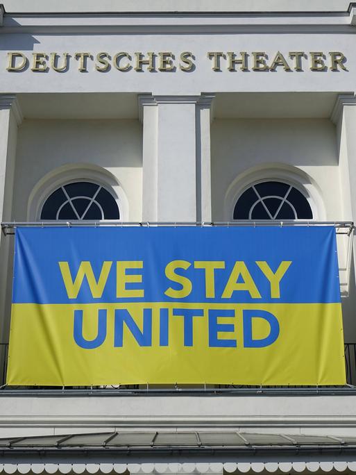 Die blau-gelbe Flagge der Ukraine mit der Aufschrift "We stay united" hängt am Deutschen Theater Berlin.