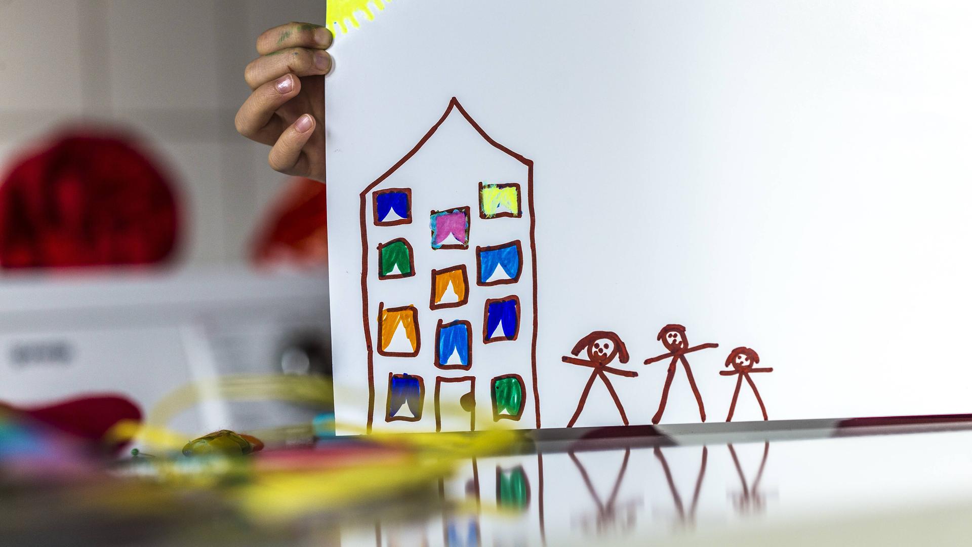 Eine Kinderhand hält eine Zeichnung von einem Haus