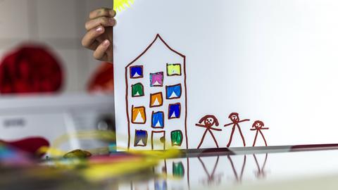 Eine Kinderhand hält eine Zeichnung von einem Haus