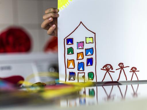 Eine Kinderhand hält eine Zeichnung von einem Haus