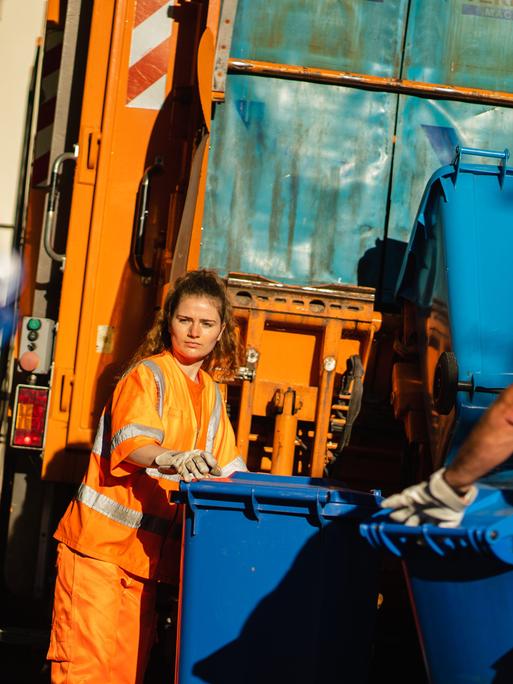 Zwei Müllwerker bei der Arbeit: Eine junge Frau und ein mittelalter Mann schieben Papiermülltonnen zum Laster der Müllabfuhr