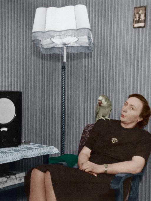 Frau mit Papagei auf der Schulter vor einem Radio ('Volksempfänger'). - Foto, undat. (30er Jahre); digital koloriert.