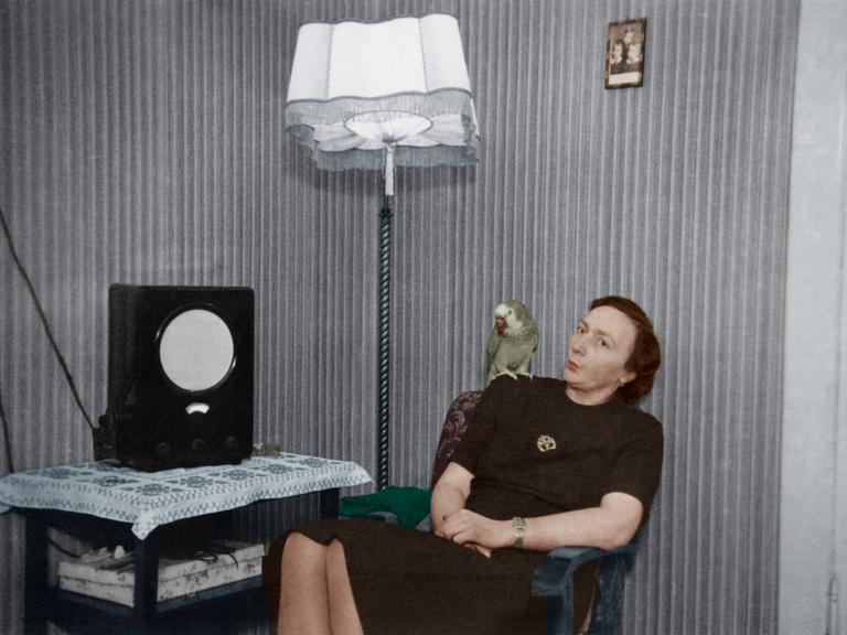 Frau mit Papagei auf der Schulter vor einem Radio ('Volksempfänger'). - Foto, undat. (30er Jahre); digital koloriert.