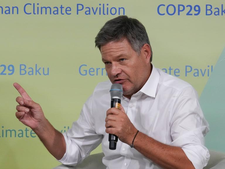 Robert Habeck spricht in ein Mikrofon, im Hintergrund ist eine Tafel mit der Aufschrift Climate Pavilion COP29.