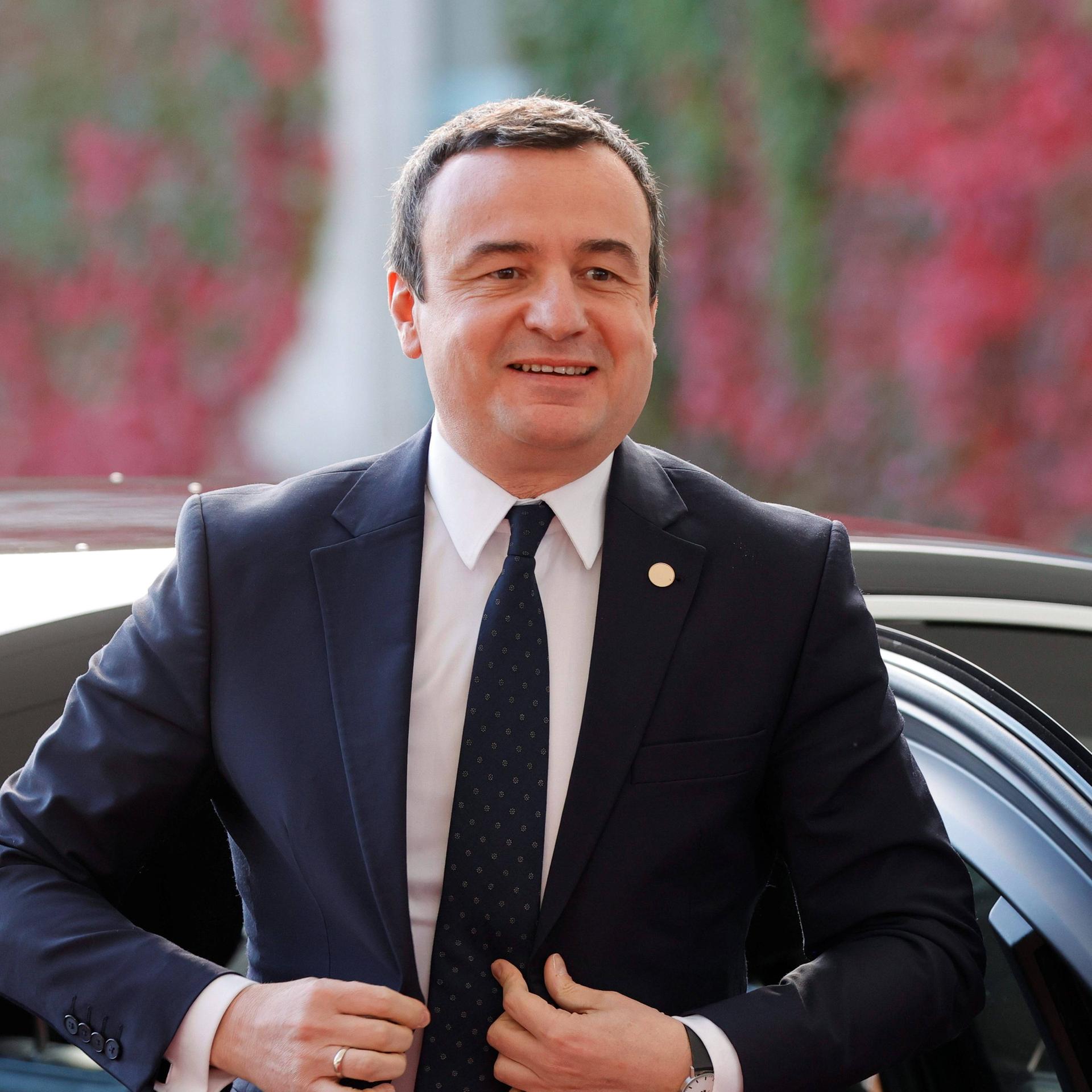 Albin Kurti, kosovarischer Premierminister, schließt den obersten Knopf seines Jacketts und lächelt in die Kamera.