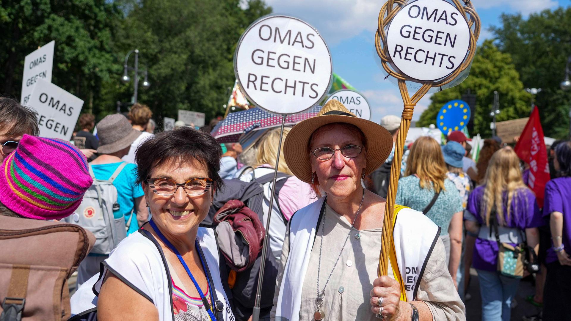 Zwei Teilnehmerinnen der Vereinigung Omas gegen rechts halten bei einer Demonstration Teppichklopfer in den Händen, die mit dem Spruch "Omas gegen Rechts" bestückt sind.