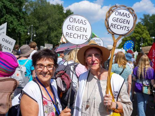 Zwei Teilnehmerinnen der Vereinigung Omas gegen rechts halten bei einer Demonstration Teppichklopfer in den Händen, die mit dem Spruch "Omas gegen Rechts" bestückt sind.