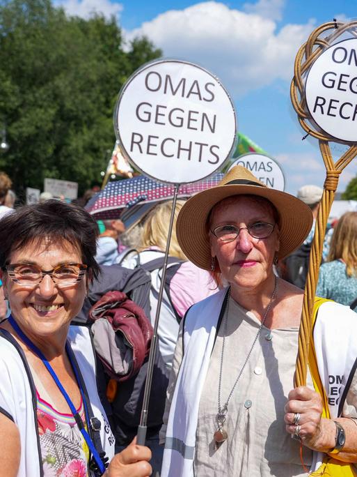 Zwei Teilnehmerinnen der Vereinigung Omas gegen rechts halten bei einer Demonstration Teppichklopfer in den Händen, die mit dem Spruch "Omas gegen Rechts" bestückt sind.