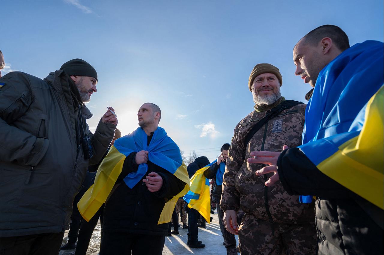 Ukrainische Soldaten stehen nach einem Gefangenenaustausch in Nationalflaggen gehüllt und in Uniform nebeneinander.