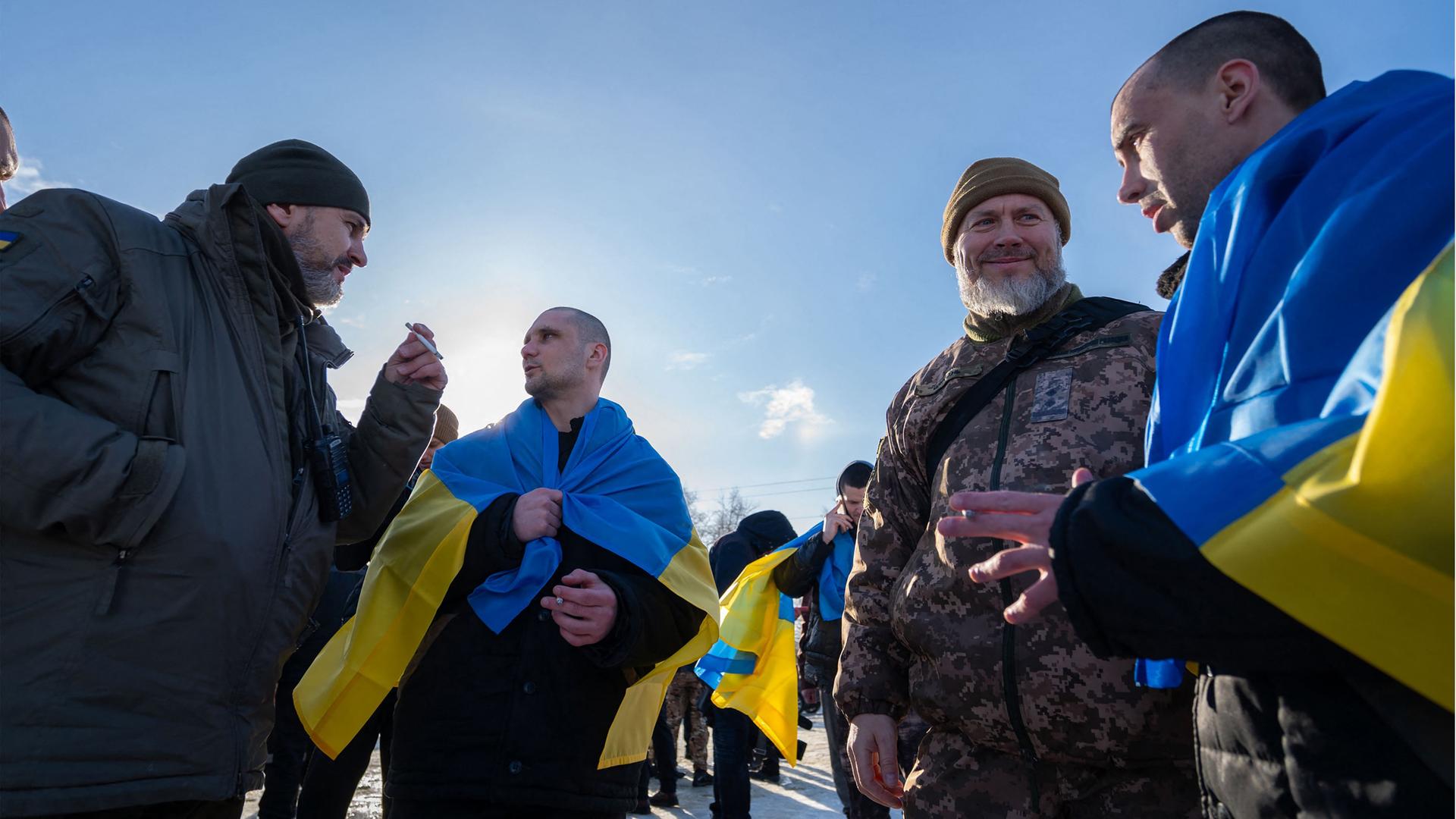 Ukrainische Soldaten stehen nach einem Gefangenenaustausch in Nationalflaggen gehüllt und in Uniform nebeneinander.