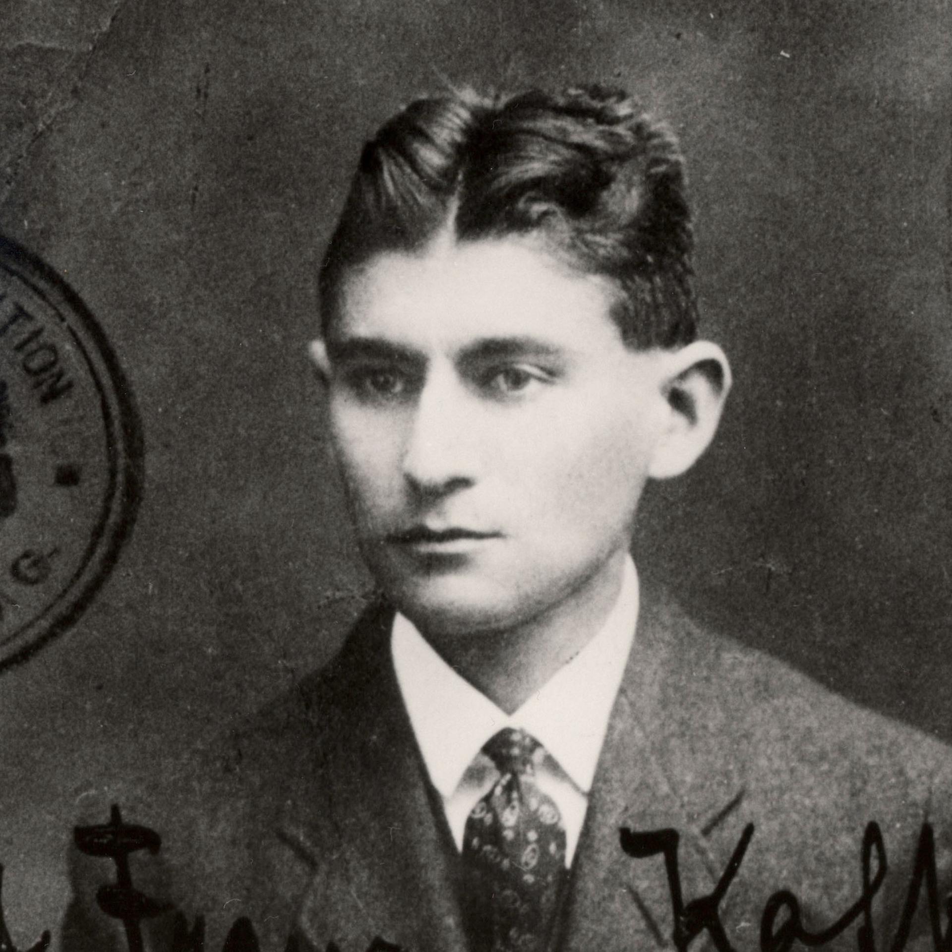 Ein schwarzweißes Passfoto zeigt Franz Kafka, der sehr ernst blickt