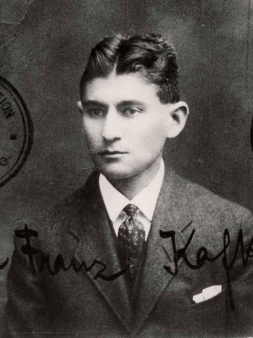 Ein schwarzweißes Passfoto zeigt Franz Kafka, der sehr ernst blickt