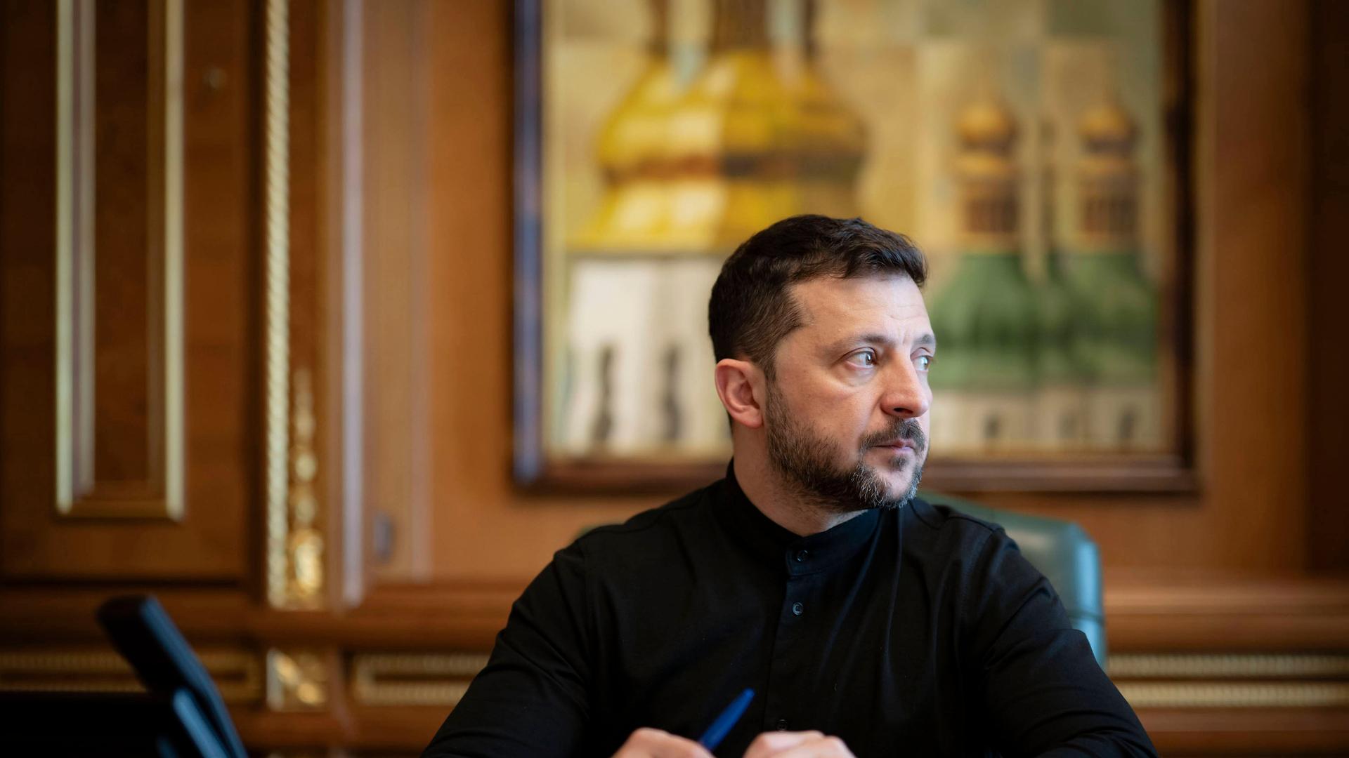 Der ukrainische Präsident Selenskyj sitzt an einem Schreibtisch und schaut ernst nach rechts Der ukrainische Präsident Selenskyj sitzt an einem Schreibtisch und schaut ernst nach rechts