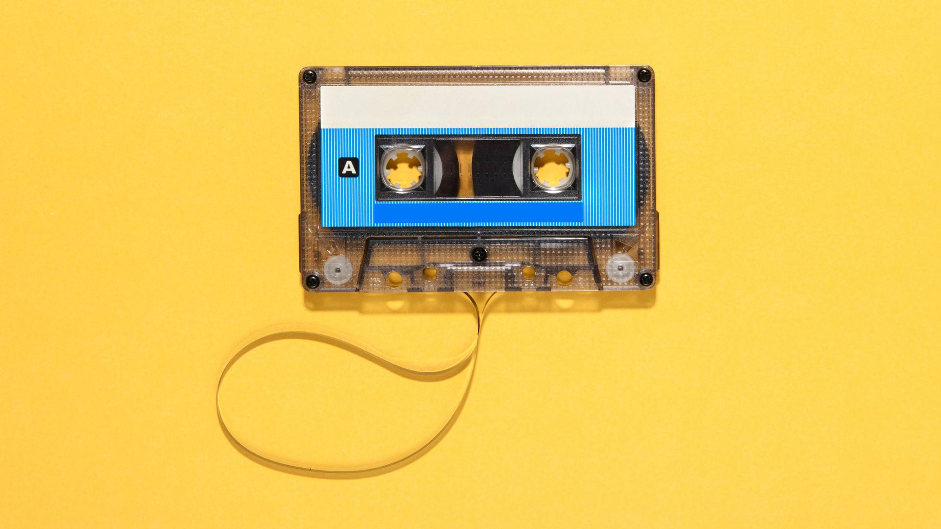 Eine Musikkassette mit heraushängendem Tonband auf gelbem Untergrund.
