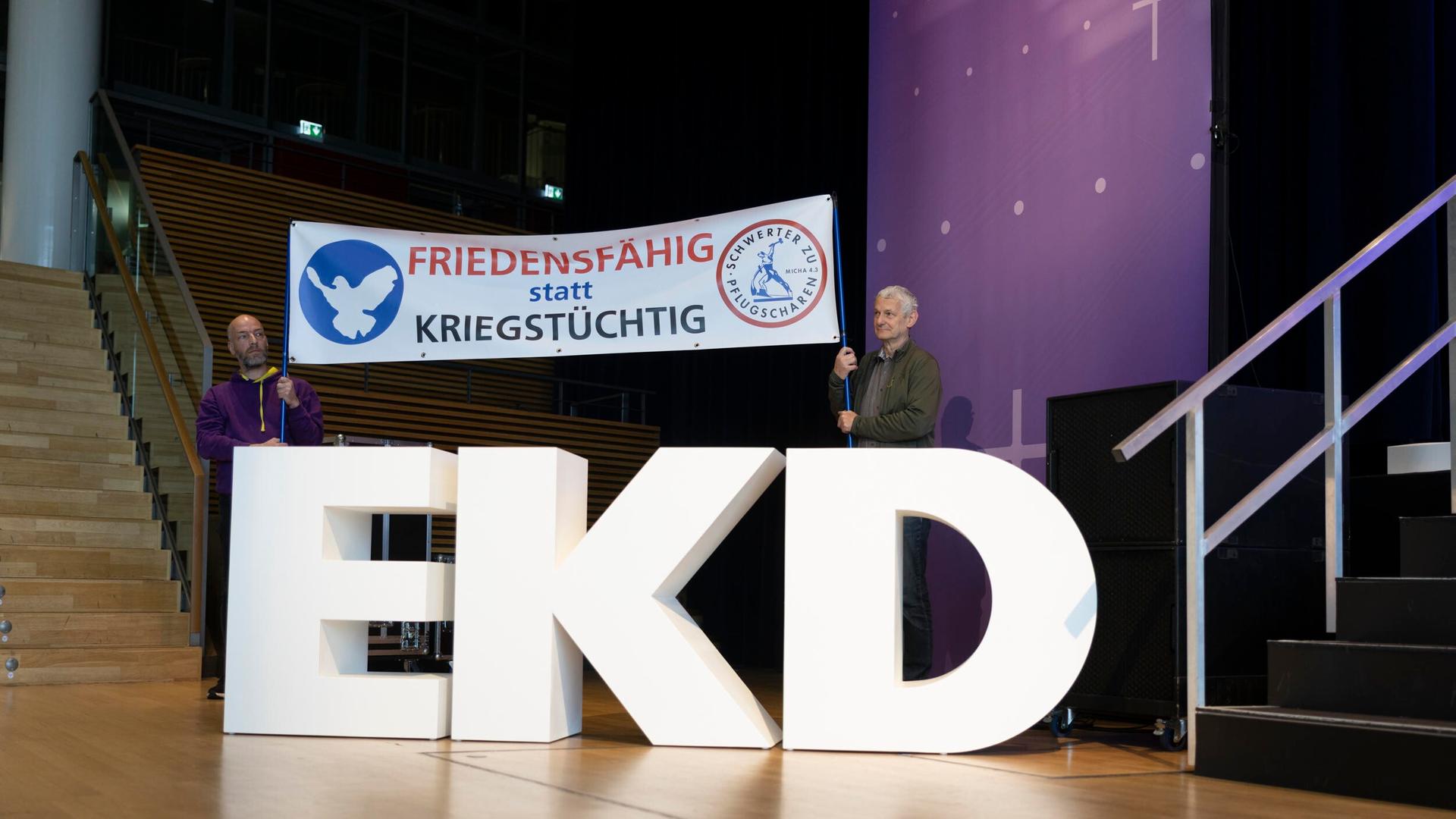 Zwei Personen halten ein Banner mit der Aufschrift "Friedensfähig statt Kriegstüchtig".